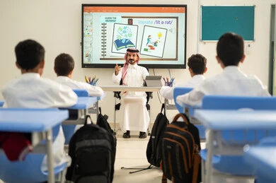 تطور طرائق التدريس في مدارس المملكة، طلاب عربيين خليجيين سعوديين يجلسون في مقاعدهم وأمامهم مدرس سعودي يستخدم جهاز التابلت، الاستفادة من التقنيات والتكنولوجيا الحديثة في التعلم والدراسة، المناهج المطورة والتعليم الالكتروني