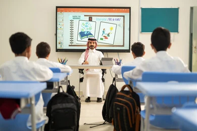الاستفادة من التقنيات والتكنولوجيا الحديثة في التعلم والدراسة، المناهج المطورة والتعليم الالكتروني،تطور طرائق التدريس في مدارس المملكة، طلاب عربيين خليجيين سعوديين يجلسون في مقاعدهم وأمامهم مدرس سعودي يستخدم جهاز التابلت