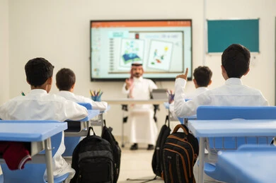 تعابير وايماءات الحماس لمعرفة الجواب الصحيح، طالب عربي خليجي سعودي مبتسم يرتدي الثوب التقليدي يرفع يديه للإجابة، التفاعل والمشاركة داخل الفصل الدراسي، التربية والتعليم بالمناهج المقررة للطلاب في المملكة العربية السعودية