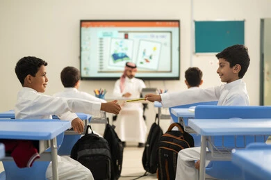 ايماءات الود والمحبه، تطور طرائق التدريس في مدارس المملكة،الاستفادة من التقنيات المتطورة في التعلم والدراسة، المناهج المطورة والتعليم الالكتروني، طالبان عربيان خليجيان سعوديان يجلسان في مقاعدهم يساعدان بعضهم البعض بتعابير وجه سعيده