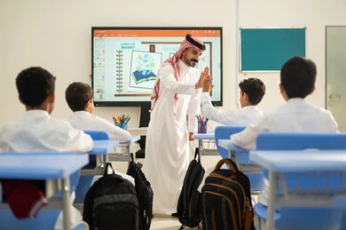 أهداف التربية والتعليم في المملكة العربية السعودية، موسم العودة إلى المدارس, طلاب عربيين خليجيين سعوديين يجلسون على المقاعد داخل الصف وينتبهون للدرس بايماءات التركيز، تنمية المهارات الإبداعية، مفهوم الاجتهاد والتفوق، مدرس سعودي يصافح طالب بتعابير السعادة