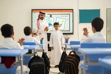 ايماءات السرور والسعادة، تعابير يد بالتميز والتفوق ،  تكريم طالب مجتهد، تطور طرائق التدريس في مدارس المملكة،الاستفادة من التقنيات المتطورة في التعلم والدراسة، المناهج المطورة والتعليم الالكتروني، طلاب عربيين خليجيين سعوديين يجلسون في مقاعدهم وأمامهم مدرس سعودي يستخدم السبورة الالكترونية