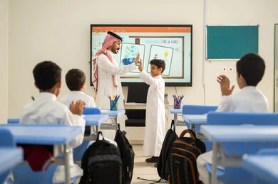 تعابير يد بالتميز والتفوق ،  تكريم طالب مجتهد، ايماءات السرور والسعادة، تطور طرائق التدريس في مدارس المملكة،الاستفادة من التقنيات المتطورة في التعلم والدراسة، المناهج المطورة والتعليم الالكتروني، طلاب عربيين خليجيين سعوديين يجلسون في مقاعدهم وأمامهم مدرس سعودي يستخدم السبورة الالكترونية