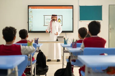تطور طرائق التدريس في مدارس المملكة،الاستفادة من التقنيات المتطورة في التعلم والدراسة، المناهج المطورة والتعليم الالكتروني، طلاب عربيين خليجيين سعوديين يجلسون في مقاعدهم وأمامهم مدرس سعودي يستخدم السبورة الالكترونية وجهاز التابلت فى الشرح