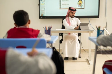 استخدام التكنولوجيا الحديثة، المناهج المطورة والتعليم الالكتروني، طلاب عربيين خليجيين سعوديين يجلسون في مقاعدهم وأمامهم مدرس سعودي يستخدم السبورة الالكترونية وجهاز التابلت فى الشرح، تطور طرائق التدريس في مدارس المملكة