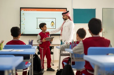 الاستفادة من التقنيات المتطورة في التعلم والدراسة، تطور طرائق التدريس في مدارس المملكة،المناهج المطورة والتعليم الالكتروني، طلاب عربيين خليجيين سعوديين يجلسون في مقاعدهم وأمامهم مدرس سعودي وطالب  يستخدم جهاز التابلت