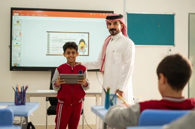 تطور طرائق التدريس في مدارس المملكة،الاستفادة من التقنيات المتطورة في التعلم والدراسة، المناهج المطورة والتعليم الالكتروني، طلاب عربيين خليجيين سعوديين يجلسون في مقاعدهم وأمامهم مدرس سعودي وطالب  يستخدم جهاز التابلت