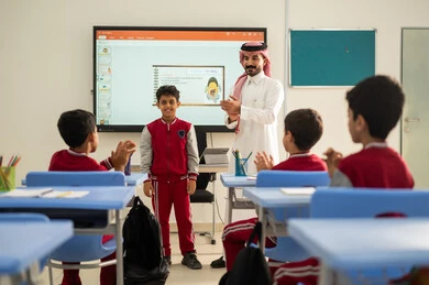 ايماءات السرور والسعادة، تعابير يد بالتميز والتفوق ،  تكريم طالب مجتهد، تطور طرائق التدريس في مدارس المملكة،الاستفادة من التقنيات المتطورة في التعلم والدراسة، المناهج المطورة والتعليم الالكتروني، طلاب عربيين خليجيين سعوديين يجلسون في مقاعدهم وأمامهم مدرس سعودي يستخدم السبورة الالكترونية