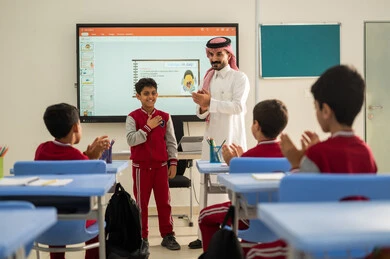 تعابير يد بالتميز والتفوق ،  تكريم طالب مجتهد، ايماءات السرور والسعادة، تطور طرائق التدريس في مدارس المملكة،الاستفادة من التقنيات المتطورة في التعلم والدراسة، المناهج المطورة والتعليم الالكتروني، طلاب عربيين خليجيين سعوديين يجلسون في مقاعدهم وأمامهم مدرس سعودي يستخدم السبورة الالكترونية
