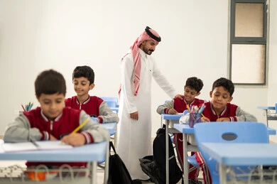 معلم عربي خليجي سعودي يرتدي الثوب التقليدي والشماغ يقوم بمناقشة الدروس مع طلابه، مجموعة من طلاب عربيين خليجيين سعوديين يرتدون الزي المدرسي يقومون بتأديه الواجبات ، المشاركة الفعالة للطلاب مع المدرسين، التربية والتعليم بالمناهج المقررة للتلاميذ، جودة التعليم في السعودية، حوارات ودية بين الاستاذ والطلاب