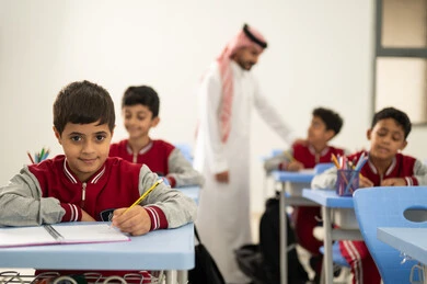 مجموعة من طلاب عربيين خليجيين سعوديين يرتدون الزي المدرسي يقومون بتأديه الواجبات ، المشاركة الفعالة للطلاب مع المدرسين، التربية والتعليم بالمناهج المقررة للتلاميذ، جودة التعليم في السعودية، معلم عربي خليجي سعودي يرتدي الثوب التقليدي والشماغ يقوم بمناقشة الدروس مع طلابه، حوارات ودية بين الاستاذ والطلاب