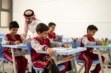 المشاركة الفعالة للطلاب مع المدرسين، جودة التعليم في السعودية، معلم عربي خليجي سعودي يرتدي الثوب التقليدي والشماغ يقوم بمناقشة الدروس مع طلابه، مجموعة من طلاب عربيين خليجيين سعوديين يرتدون الزي المدرسي يقومون بتأديه الواجبات ، التربية والتعليم بالمناهج المقررة للتلاميذ، حوارات ودية بين الاستاذ والطلاب