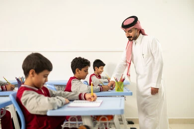 Active participation of students with teachers, quality of education in Saudi Arabia, a Gulf Arab Saudi teacher wearing traditional attire and a shemagh discussing lessons with his students, a group of Gulf Arab Saudi students wearing school uniforms doing their homework, education and teaching with the prescribed curricula for students, friendly dialogues between the teacher and students.