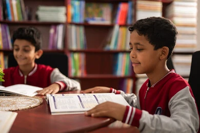 مفهوم التعليم الذاتي ، بيئة تعليمية متطورة، تأدية الواجبات المدرسية ، طلاب عربيين سعوديين خليجيين يرتدون الزي المدرسي يجلسون في المكتبة المدرسية ، الاستمتاع بقراءة الكتب المدرسية، التعليم في المملكة العربية السعودية