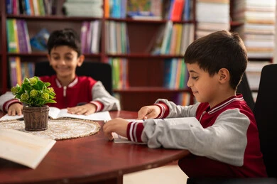 Two Arab Saudi Gulf students wearing school uniforms are sitting in the school library, enjoying reading textbooks, education in the Kingdom of Saudi Arabia, the concept of self-education, an advanced educational environment, and completing school assignments.