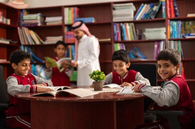 التعليم في المملكة العربية السعودية، تأدية الواجبات المدرسية، معلم عربي خليجي سعودي يقوم بمساعده طلابه، الحوارات الودية بين المعلم والطالب ، طلاب عربيين سعوديين خليجيين يرتدون الزي المدرسي يجلسون في المكتبة المدرسية برفقة معلمهم ، الاستمتاع بقراءة الكتب المدرسية