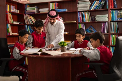 مفهوم التعليم والثقافة، تأدية الواجبات المدرسية، معلم عربي خليجي سعودي يقوم بمساعده طلابه، الحوارات الودية بين المعلم والطالب ، طلاب عربيين سعوديين خليجيين يرتدون الزي المدرسي يجلسون في المكتبة المدرسية برفقة معلمهم ، التعليم في المملكة العربية السعودية