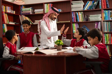 تأدية الواجبات المدرسية، معلم عربي خليجي سعودي يقوم بمصافحة طالب ، الحوارات الودية بين المعلم والطالب ، طلاب عربيين سعوديين خليجيين يرتدون الزي المدرسي يجلسون في المكتبة المدرسية برفقة معلمهم ، الاستمتاع بقراءة الكتب المدرسية، التعليم في المملكة العربية السعودية