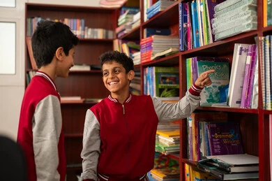 مفهوم التعليم الذاتي, بيئه مدرسيه تعليميه متطوره ، ممارسة هوايه المطالعة، مجموعة من طلاب عربيين خليجيين سعوديين يرتدون الزي المدرسي يجلسون في المكتبة المدرسية، الاستمتاع بقراءة الكتب المدرسية، التعليم في المملكة العربية السعودية