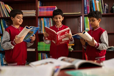 A developed educational school environment, the concept of self-learning, practicing the hobby of reading, a group of Arab Gulf Saudi students wearing school uniforms sitting in the school library, enjoying reading school books, education in the Kingdom of Saudi Arabia.
