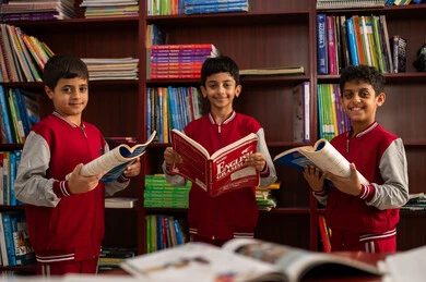 The concept of self-education, an advanced educational school environment, practicing the hobby of reading, a group of Arab Gulf Saudi students wearing school uniforms sitting in the school library, enjoying reading school books, education in the Kingdom of Saudi Arabia.
