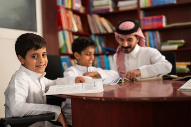 التعليم في المملكة العربية السعودية، تأدية الواجبات المدرسية، الحوارات الودية بين المعلم والطالب ، طلاب عربيين سعوديين خليجيين يرتدون الزي التقليدي يجلسون في المكتبة المدرسية برفقة معلمهم ، الاستمتاع بقراءة الكتب المدرسية