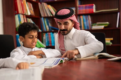 Friendly dialogues between the teacher and the student, a Saudi Gulf Arab student sitting in the school library with their teacher, enjoying reading school books, completing school assignments, education in the Kingdom of Saudi Arabia.