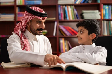 Enjoying reading school books, doing homework, friendly dialogues between the teacher and the student, a Saudi Gulf Arab student sitting in the school library with their teacher, education in the Kingdom of Saudi Arabia.