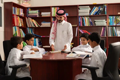 التعليم في المملكة العربية السعودية، الحوارات الودية بين المعلم والطالب ، طلاب عربيين سعوديين خليجيين يجلسون في المكتبة المدرسية برفقة معلمهم ، الاستمتاع بقراءة الكتب المدرسية، تأدية الواجبات المدرسية