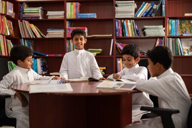 مفهوم التعليم الذاتي, بيئه مدرسيه تعليميه متطوره ، ممارسة هوايه المطالعة، مجموعة من طلاب عربيين خليجيين سعوديين يرتدون الزي التقليدي يجلسون في المكتبة المدرسية، الاستمتاع بقراءة الكتب المدرسية، التعليم في المملكة العربية السعودية