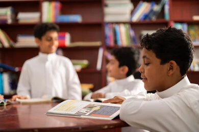 مفهوم التعليم والثقافة , بيئه مدرسيه تعليميه متطوره ، ممارسة هوايه المطالعة، مجموعة من طلاب عربيين خليجيين سعوديين يرتدون الزي التقليدي يجلسون في المكتبة المدرسية، الاستمتاع بقراءة الكتب المدرسية، التعليم في المملكة العربية السعودية