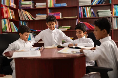 الاستمتاع بقراءة الكتب المدرسية، مفهوم التعليم الذاتي, بيئه مدرسيه تعليميه متطوره ، ممارسة هوايه المطالعة، مجموعة من طلاب عربيين خليجيين سعوديين يرتدون الزي التقليدي يجلسون في المكتبة المدرسية، التعليم في المملكة العربية السعودية