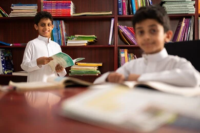 The concept of self-education, an advanced educational school environment, practicing the hobby of reading, a group of Arab Gulf Saudi students wearing traditional attire sitting in the school library, enjoying reading school books, education in the Kingdom of Saudi Arabia.