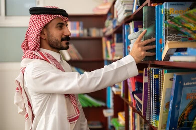 Practicing the hobby of reading, education in the Kingdom of Saudi Arabia, a Saudi Arabic teacher taking a book from a wooden library in the school library, enjoying reading school books. Practicing the hobby of reading, education in the Kingdom of Saudi Arabia, a Saudi Arabic teacher taking a book from a wooden library in the school library, enjoying reading school books.