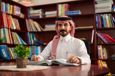التعليم في المملكة العربية السعودية، مفهوم المطالعة والثقافة ،ممارسة الهوايات المفضلة ، معلم عربي سعودي يرتدي الزى التقليدي والشماغ يجلس في المكتبة المدرسية، الاستمتاع بقراءة الكتب المفيدة