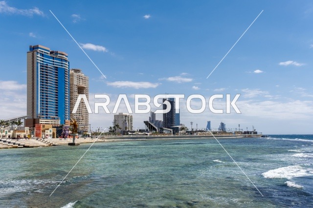 The meeting of the clear blue waters of the Red Sea with the wide horizon creates a charming daytime scene of Jeddah's beach and its distinctive landmarks, including mosques, hotels, and parks along the waterfront. The tranquil atmosphere reflects the beauty of the city of Jeddah and the splendor of its coastal nature.