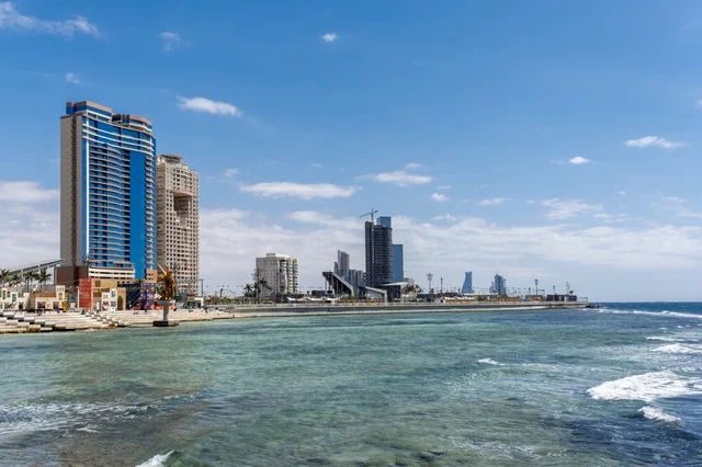 التقاء مياه البحر الأحمر الزرقاء الصافية مع الأفق الواسع، مشهد نهاري ساحر لشاطئ جدة ومعالمها المميزة ،  مساجد وفنادق ومنتزهات على الواجهة البحرية، أجواء هادئة تعكس جمال مدينة جدة وروعة طبيعتها الساحلية.