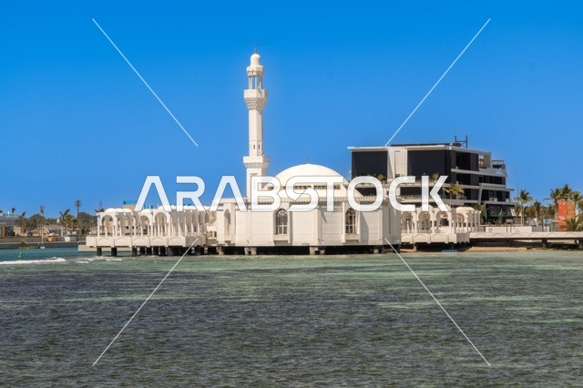 The meeting of the clear blue waters of the Red Sea with the wide horizon creates a charming daytime scene of Jeddah's beach and its distinctive landmarks, including mosques, hotels, and parks along the waterfront. The tranquil atmosphere reflects the beauty of the city of Jeddah and the splendor of its coastal nature.