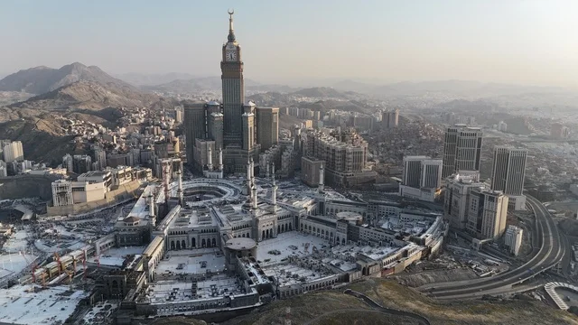 The call of Muslims to perform prayer, an aerial view of the Grand Mosque in Mecca, pilgrims gathering in the outer courtyard of the mosque, a place and a sacred religious landmark in the Kingdom of Saudi Arabia, performing the rituals of Hajj and Umrah, architectural art in the Islamic style.
