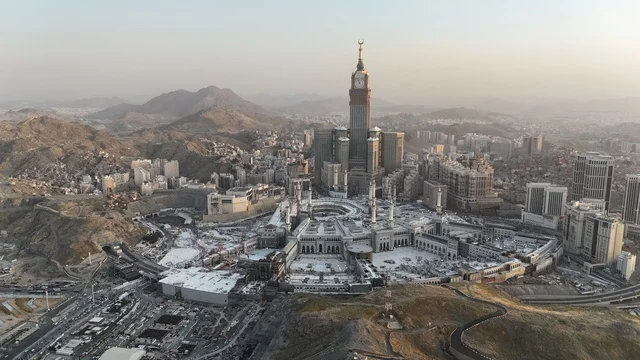 The call of Muslims to perform prayer, an aerial view of the Grand Mosque in Mecca, pilgrims gathering in the outer courtyard of the mosque, a place and a sacred religious landmark in the Kingdom of Saudi Arabia, performing the rituals of Hajj and Umrah, architectural art in the Islamic style.