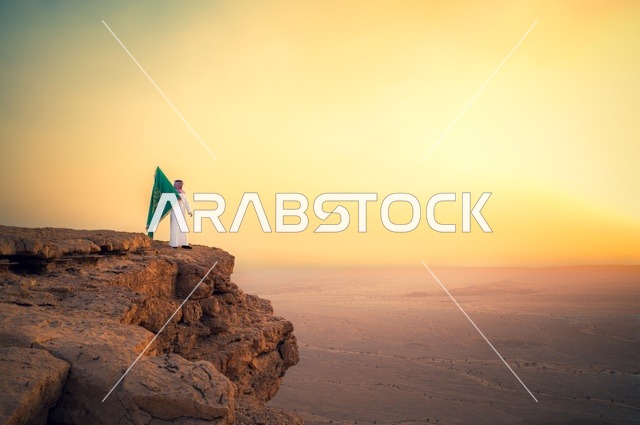 رفع علم المملكة العربية السعودية وسط الصحراء، راية التوحيد وشعار الوطن، الاحتفال بالمناسبات والأعياد الوطنية، يوم العلم 11 مارس، اليوم الوطني السعودي 23 سبتمبر، صورة من الخلف لرجل عربي خليجي سعودي يرتدي الشماغ والثوب التقليدي يعتز بتراب الوطن