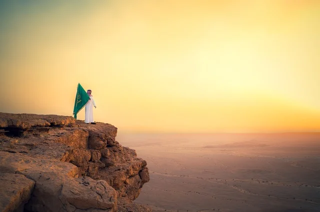 رفع علم المملكة العربية السعودية وسط الصحراء، راية التوحيد وشعار الوطن، الاحتفال بالمناسبات والأعياد الوطنية، يوم العلم 11 مارس، اليوم الوطني السعودي 23 سبتمبر، صورة من الخلف لرجل عربي خليجي سعودي يرتدي الشماغ والثوب التقليدي يعتز بتراب الوطن رفع علم المملكة العربية السعودية وسط الصحراء، راية التوحيد وشعار الوطن، الاحتفال بالمناسبات والأعياد الوطنية، يوم العلم 11 مارس، اليوم الوطني السعودي 23 سبتمبر، صورة من الخلف لرجل عربي خليجي سعودي يرتدي الشماغ والثوب التقليدي يعتز بتراب الوطن