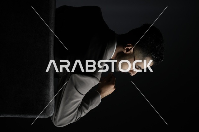  رجل  سعودي  يرتدي بدلة كلاسيكية ونظارات أنيقة، يجلس بهدوء في خلفية مظلمة، تعبير عن الوقار، التفكير العميق، واتخاذ القرارات الحاسمة