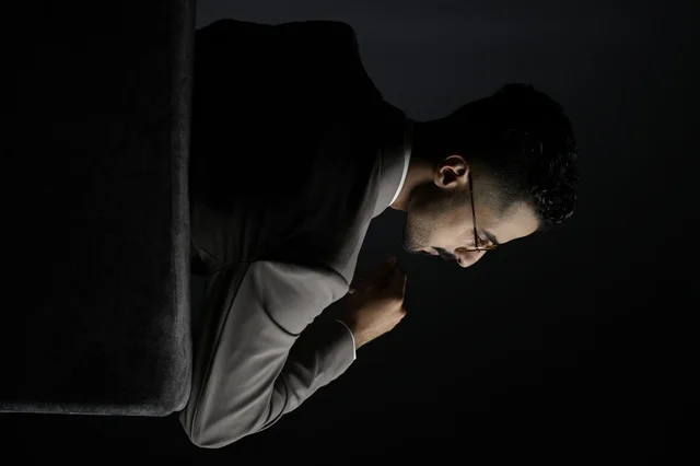  رجل  سعودي  يرتدي بدلة كلاسيكية ونظارات أنيقة، يجلس بهدوء في خلفية مظلمة، تعبير عن الوقار، التفكير العميق، واتخاذ القرارات الحاسمة