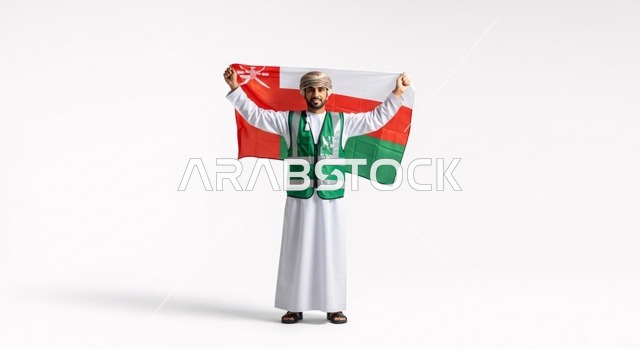 صورة كاملة لرجل عماني يرتدي الزي التقليدي وسترة أمان، يحمل بفخر علم سلطنة عمان الوطني على خلفية بيضاء.