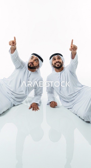 رجلان يرتديان الزي الإماراتي التقليدي يشيران بأصابعهما السبابة إلى الأعلى، معزولان على خلفية بيضاء.