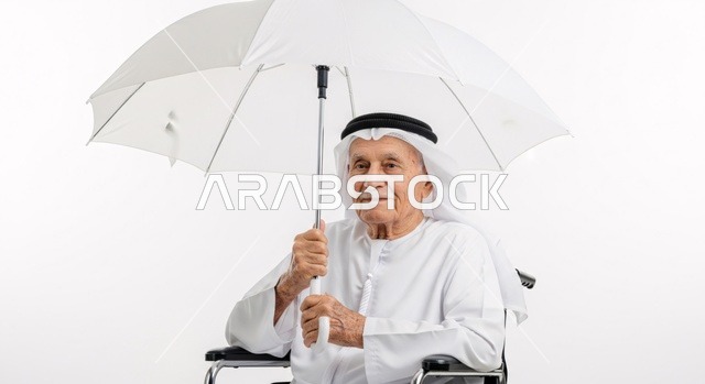 النظر الى الكاميرا بايماءات السعاده ، رجل عربي مسن يجلس على كرسي متحرك يمسك بيده  مظلة