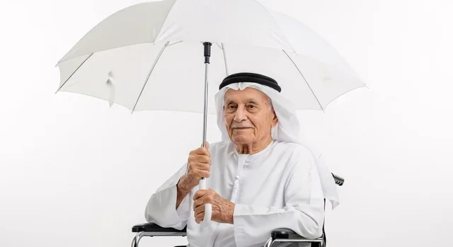 النظر الى الكاميرا بايماءات السعاده ، رجل عربي مسن يجلس على كرسي متحرك يمسك بيده  مظلة