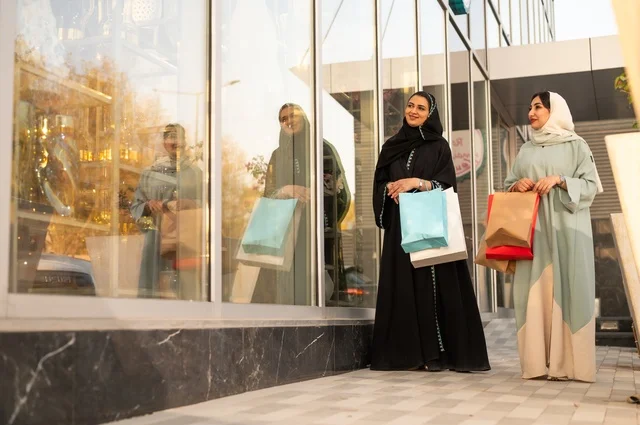 الشراء في أيام التنزيلات والتخفيضات، الاستمتاع بالشراء من المول، متعة التسوق في الجمعه البيضاء مع الاصدقاء، سيدتان عربيتان خليجيتان سعوديتان ترتديان العباءه والحجاب تحملان حقائب التسوق بتعابير وايماءات السعادة والسرور