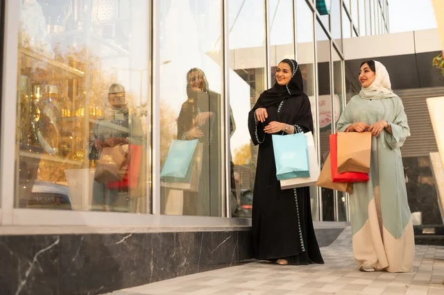 الشراء في أيام التنزيلات والتخفيضات، الاستمتاع بالشراء من المول، متعة التسوق في الجمعه البيضاء مع الاصدقاء، سيدتان عربيتان خليجيتان سعوديتان ترتديان العباءه والحجاب تحملان حقائب التسوق بتعابير وايماءات السعادة والسرور